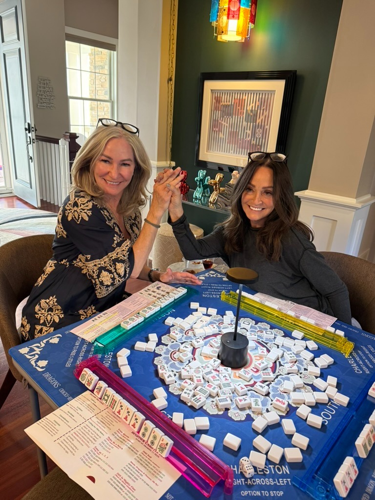 Two women holding hands and playing Mah Jongg together at a table